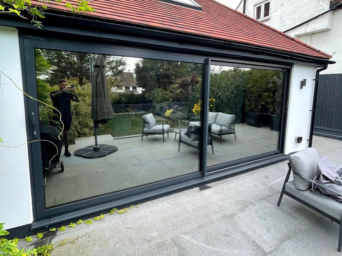 Solar film on large grey sliding doors, the glass reflecting the garden and patio furniture
